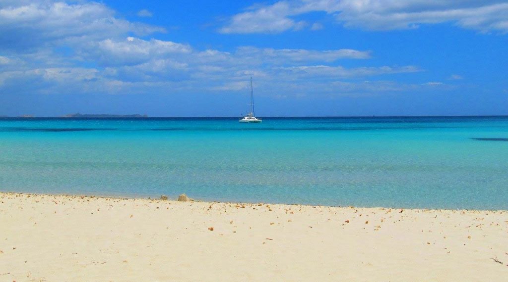 Il mare della Sardegna, con la spiaggia vuota e una barca a vela in rada