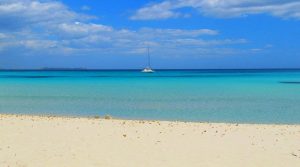 Il mare della Sardegna, con la spiaggia vuota e una barca a vela in rada